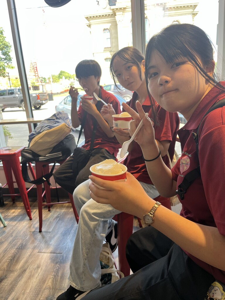 Three individuals wearing matching red shirts seated on chairs, eating ice cream from red cups.