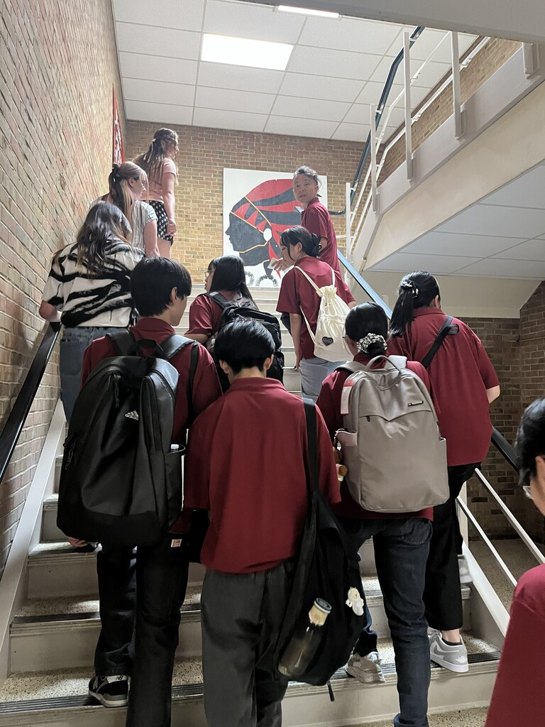 A group of students wearing maroon shirts and backpacks, ascending a staircase with brick walls.