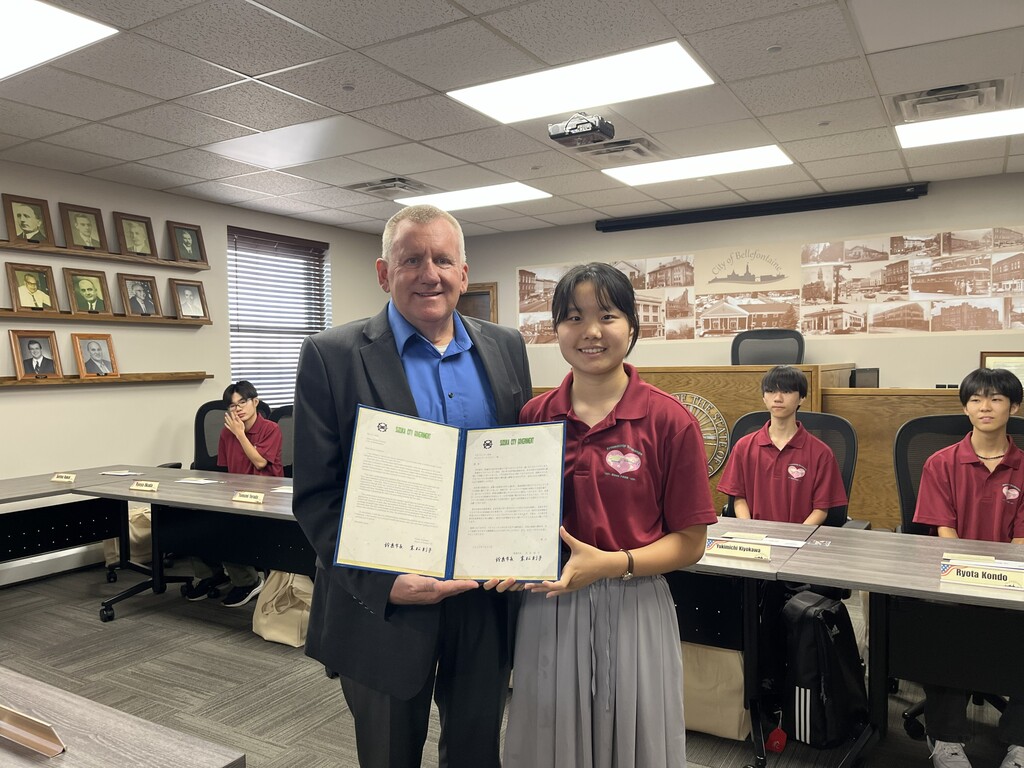 A person in a suit and a person in a maroon shirt hold an open document in a classroom.