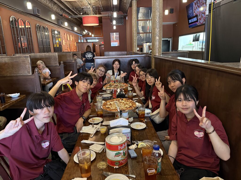 A group in maroon shirts poses for a photo at a restaurant table with a large pizza.