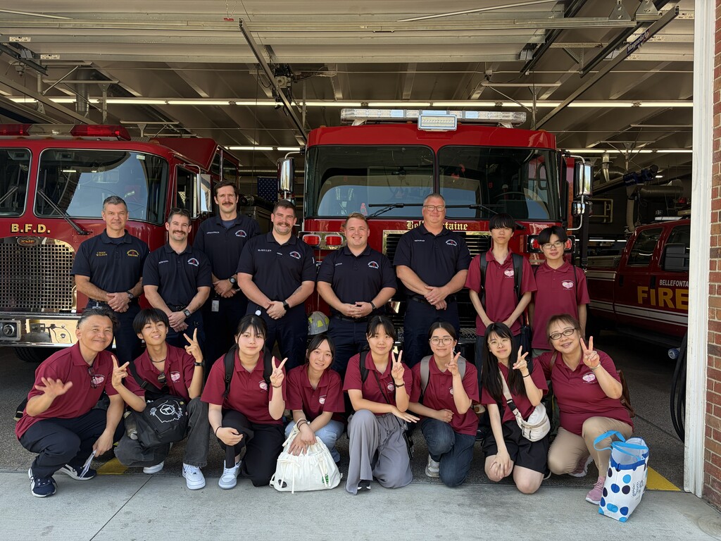 Group of people in matching red shirts, posing for a photo in front of red fire trucks.