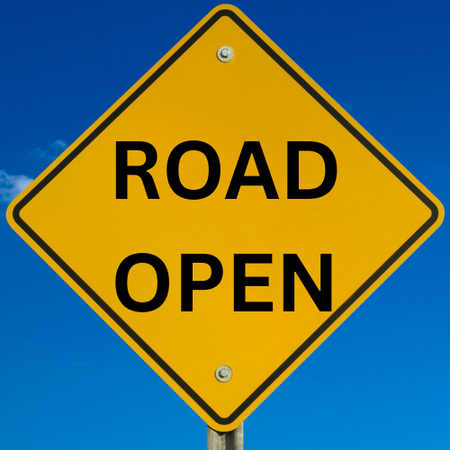 A yellow diamond-shaped sign with "ROAD OPEN" in black letters against a blue sky background.