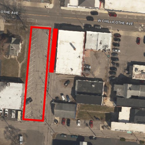 Aerial view of commercial area with multiple buildings, road, parking lot, and vehicles parked.