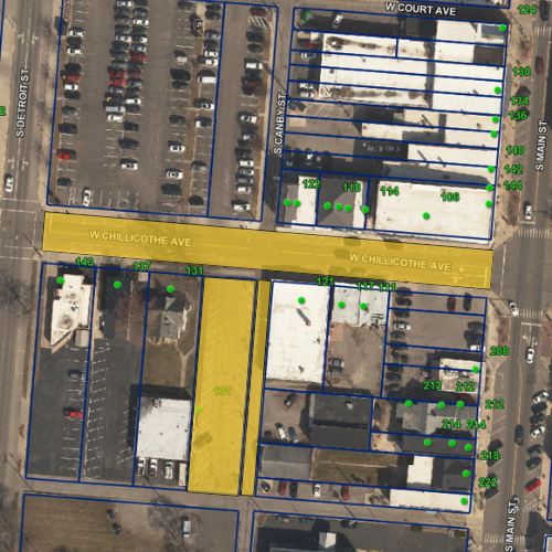 Aerial view of a city block with parking lots, buildings, and yellow and blue lines marking specific areas.