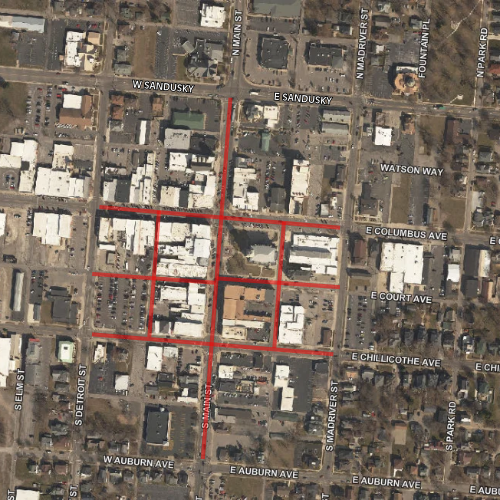 An aerial view of a city grid shows numerous buildings with roads and a red square highlighting central structures.