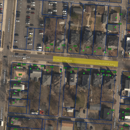 Aerial view of a neighborhood with numerous buildings, roads, and parking lots, outlined in blue lines.