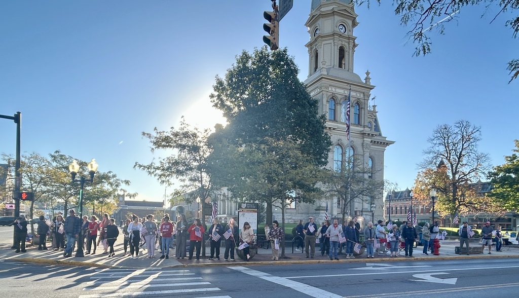 A group of people stands on a city street in front of a building with a clock tower.