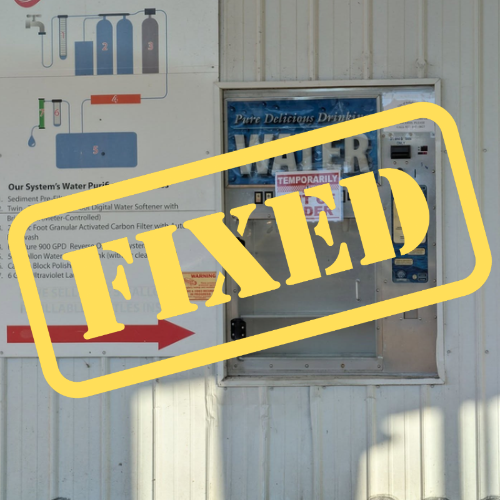 A white wall with a yellow sticker reading "FIXED" covers a water dispenser with a blue label.