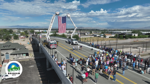 a crowd of people on the new overpass, in front of a large American flag suspended between two ladder trucks