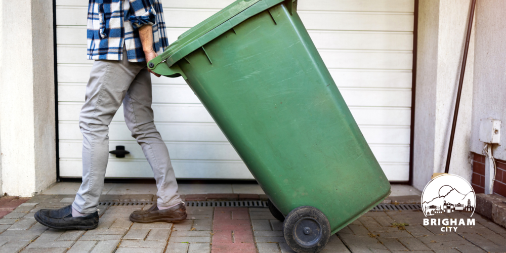 a person pulling a green garbage can in front of a garage