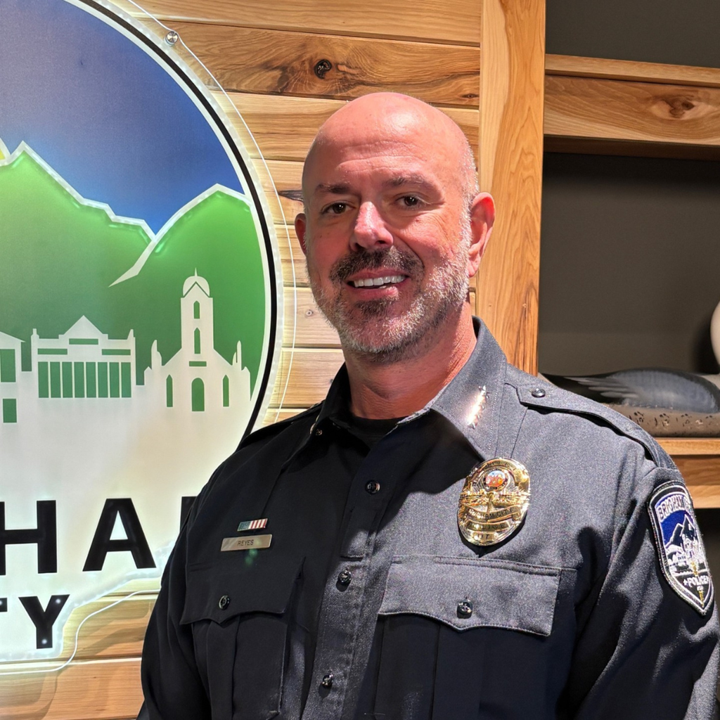 Chief Reyes stands in front of a lit-up Brigham City logo sign