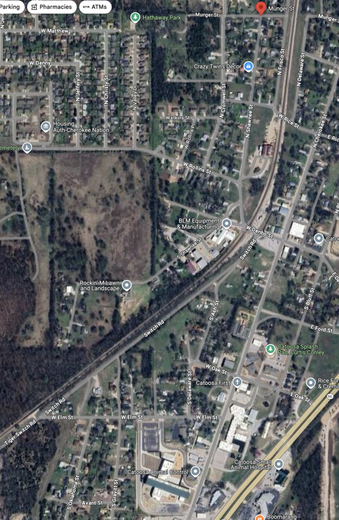 Aerial view of current day Catoosa, Oklahoma featuring streets, residential neighborhoods, and a railway line. Various buildings and green spaces are visible, along with marked locations for pharmacies.
