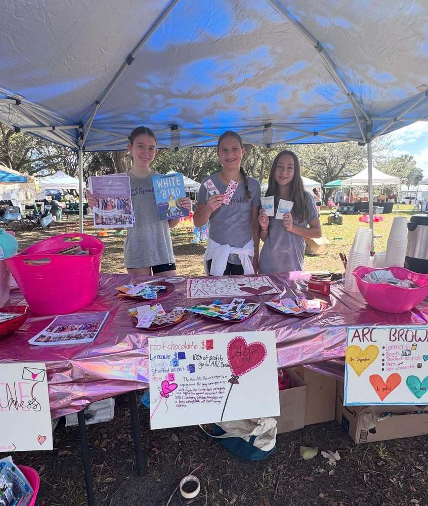 Teenagers volunteering at a fundraising tent with a table filled with artwork