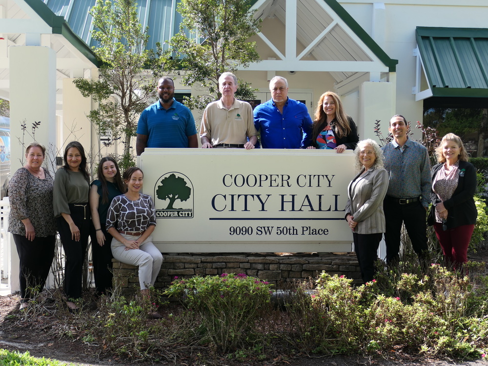 Finance Department team members standing to the side and behind the Cooper City City Hall sign.