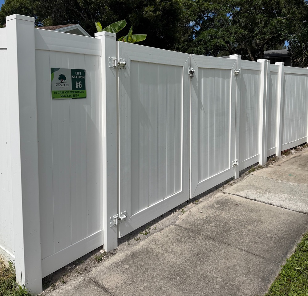 White fence and sidewalk with signage denoting Cooper City Lift Station #6