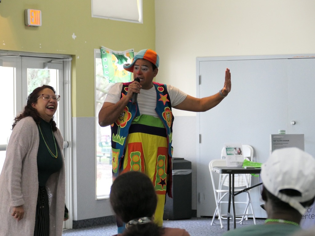 Man dressed as a clown holding a microphone as a woman laughs next to him.