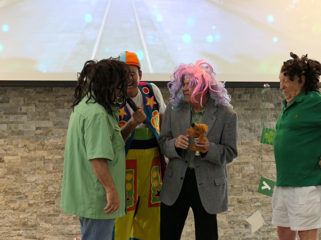 Two men wearing wigs and speaking into a microphone held by a man dressed as a clown.