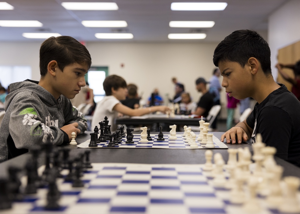Two boys concentrating and looking at a chess board as they play chess.