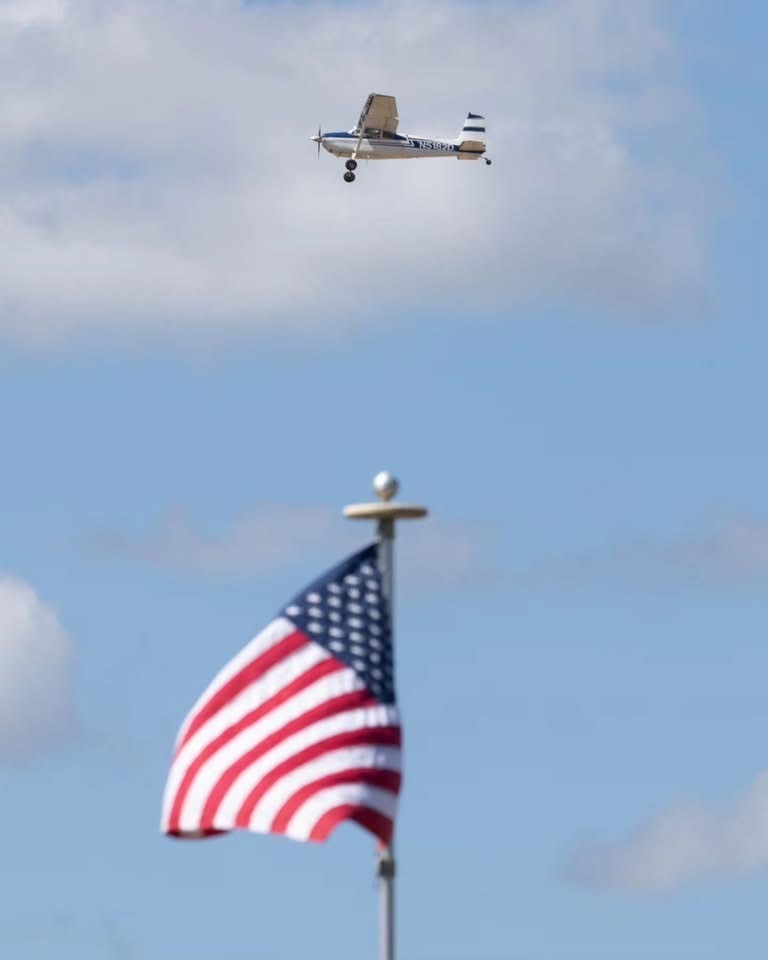 An image of one of the STOL airplanes flying above the American Flag at the Creswell Airport. 