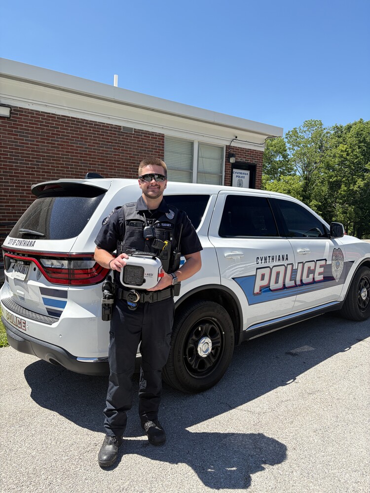 Officer Pierce Tussey holding AED in front of cruiser