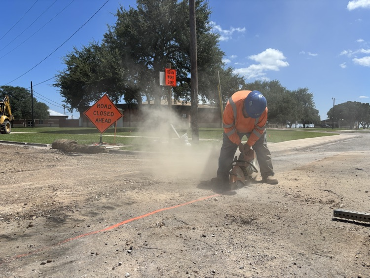 A worker cuts the old pavement at the corner of Miracle and W. Gayle, by the Edna High School auditorium .