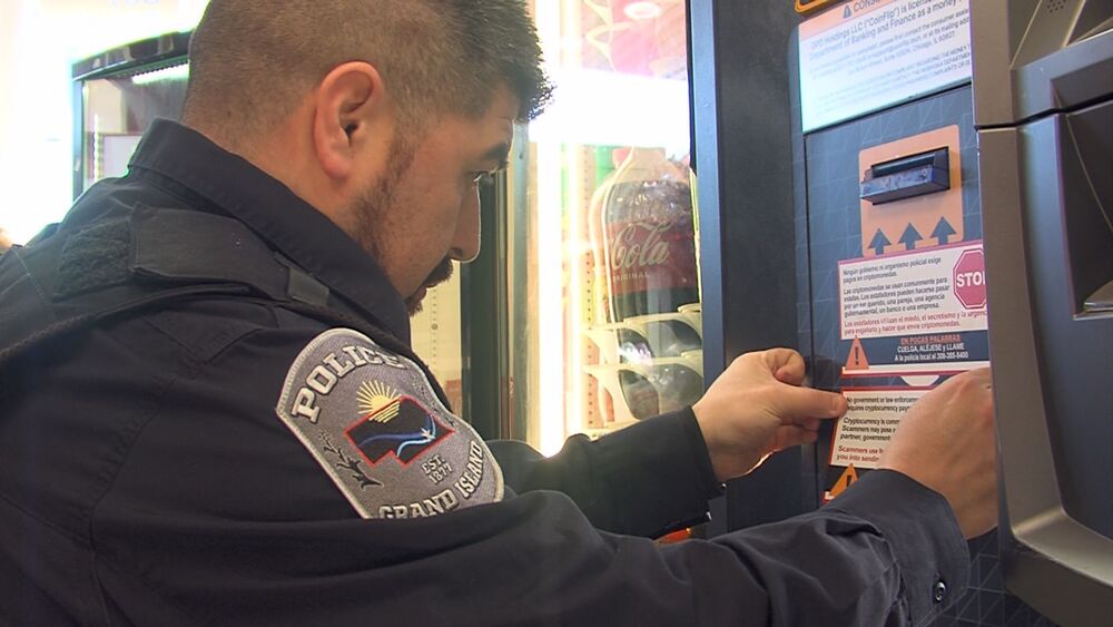 GIPD Officer putting a Crytocurrency Scam Warning Sticker on ATM