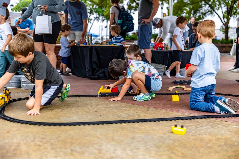 Several kids playing with toy trains on a track on the ground at the Greer City Park Amphitheater