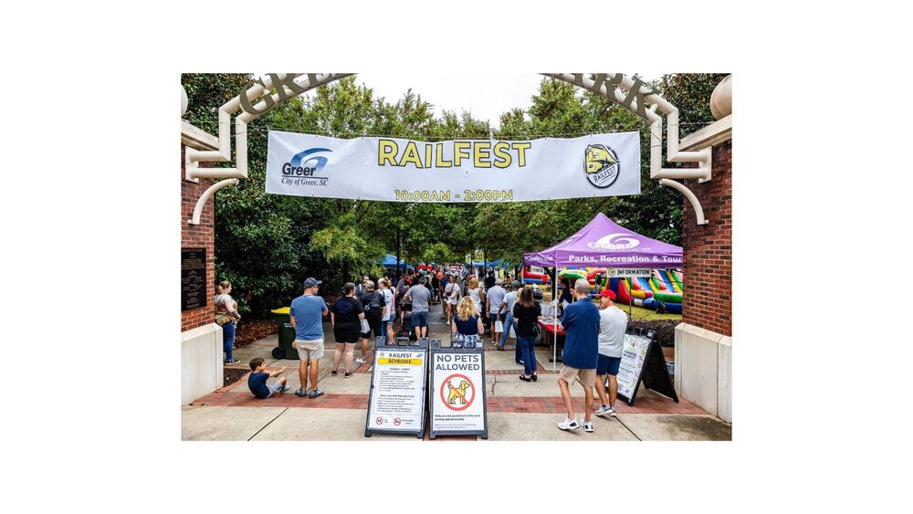 Banner hanging over the entrance to Greer City Park says Railfest 10 a.m. to 2 p.m.; you can see people and tents just inside the entrance