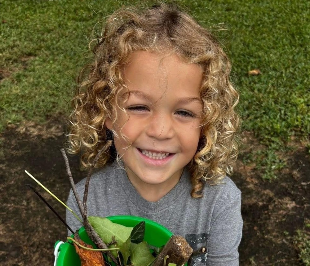 Picture of little girl holding a green bucket full of sticks and leaves