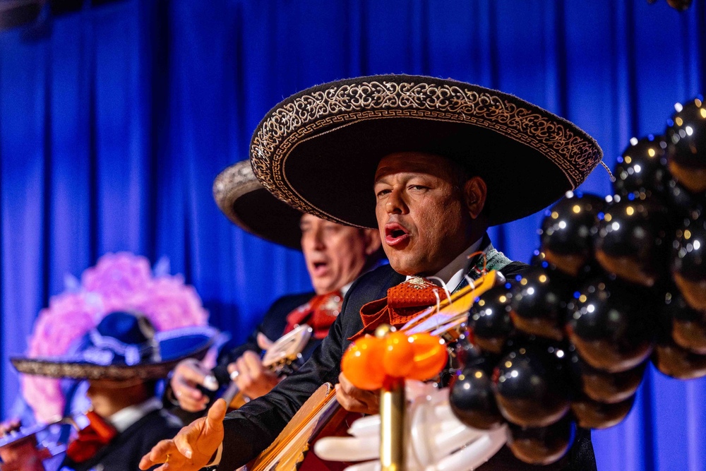 two men wearing sobreros playing stringed instruments on a stage with a blue curtain behind them