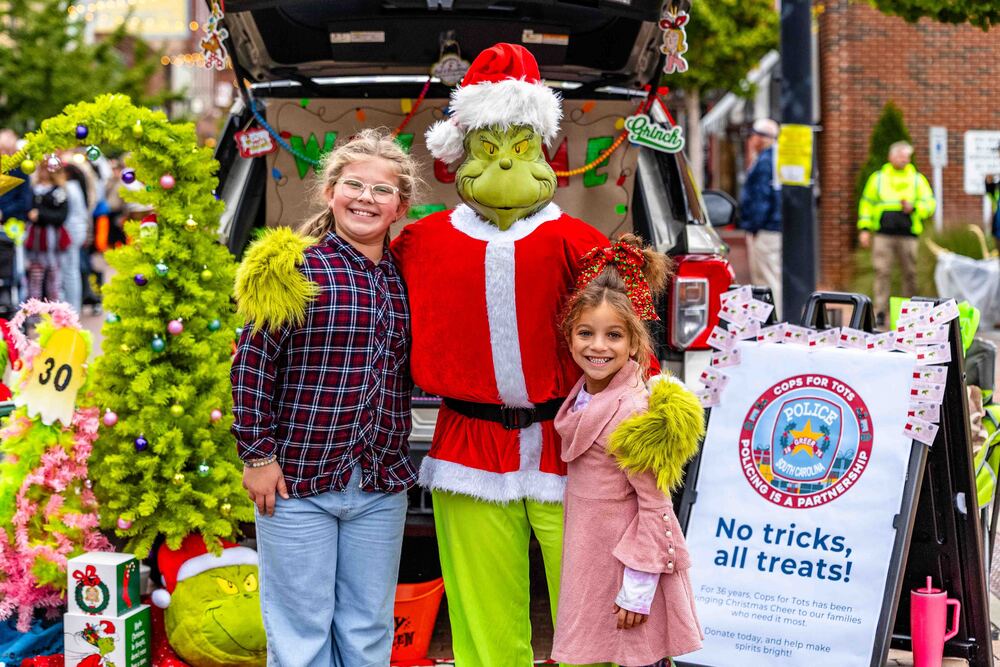 Two girls on either side of person dressed up as the Grinch in front of a "trunk" at the 2025 Trunk or Treat on Trade event