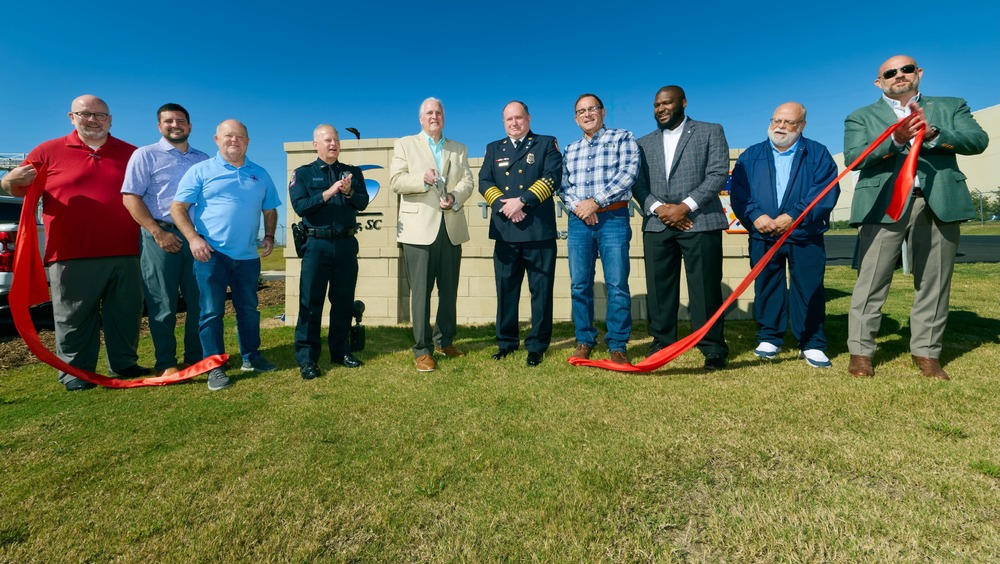 Line of men from Greer City Council, police and fire chiefs cutting a ceremonial red ribbon in front of the sign of the new Public Safety Training Center