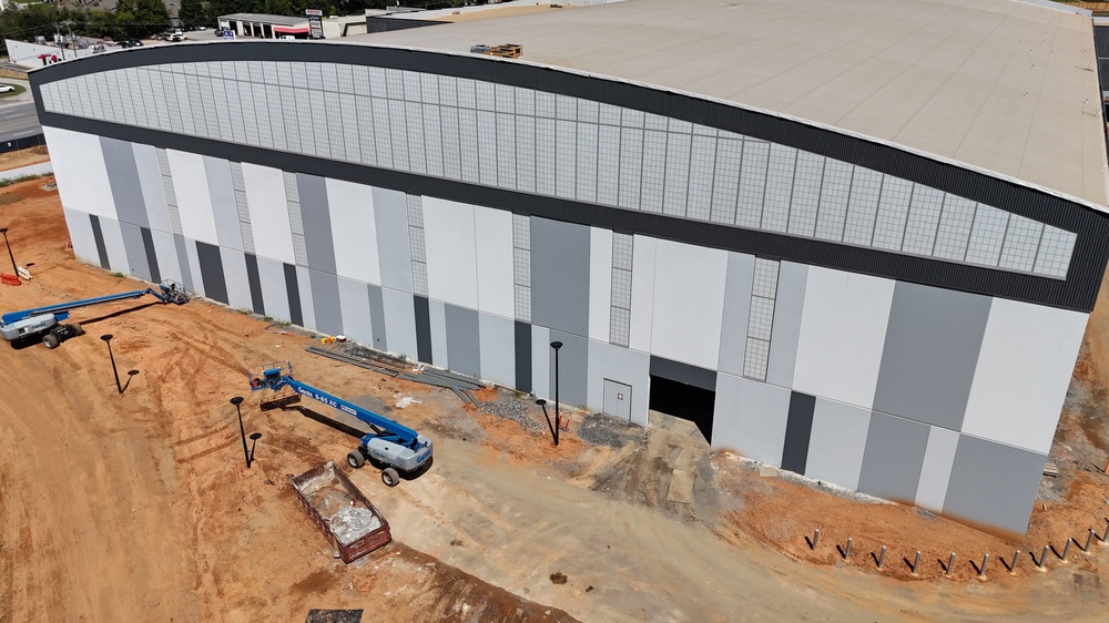 Drone shot of the final wall of windows of the city's new sports and events center; facility has a rounded roof on that side with concrete panels in various shades of gray