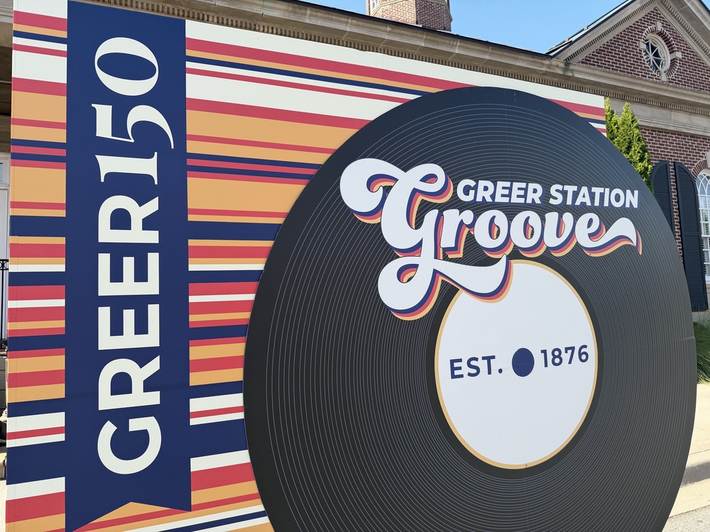 Backdrop with different colored stripes and a large image of a vinyl record. Says Greer150 Greer Station Groove, est. 1876