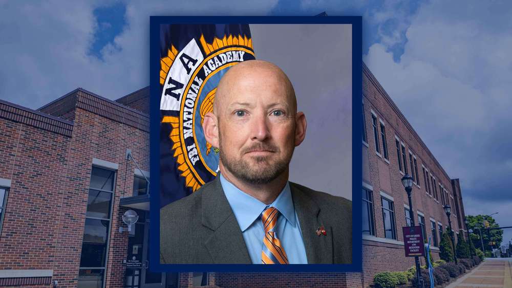 Photo of Lt. Chris Forrester in front of the FBI National Academy flag with the Greer Police Department in the Background