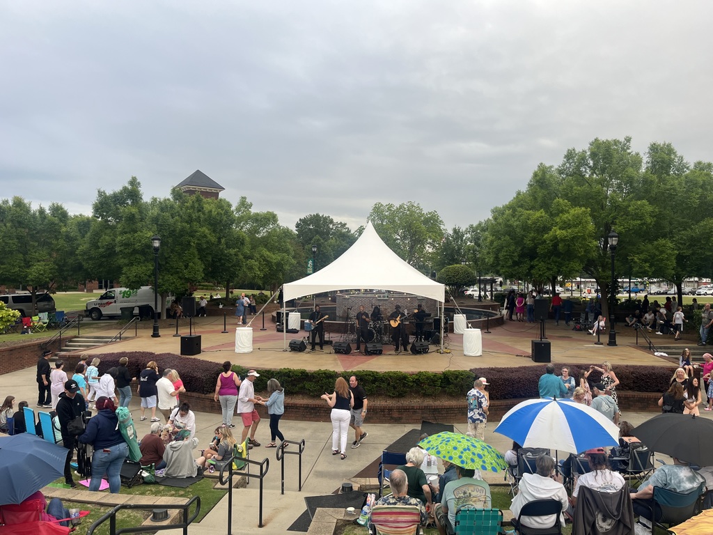 Wide shot of band on stage and people dancing during Tunes in the Park