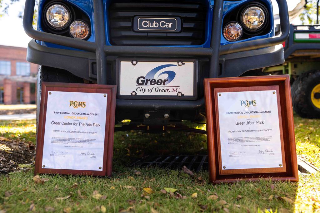 Two PGMS awards lean up against the front of a Greer Urban Parks Club Car 