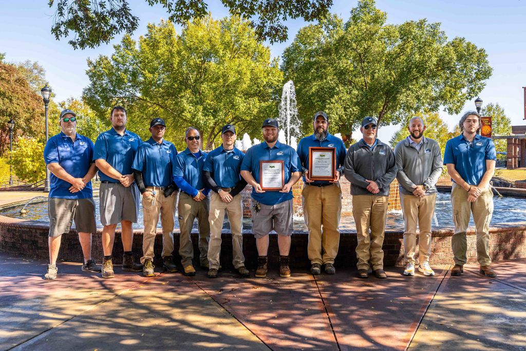 The City of Greer Urban Parks team pose for a photo holding the 2025 PGMS awards that they won with the Greer City Park fountain behind them