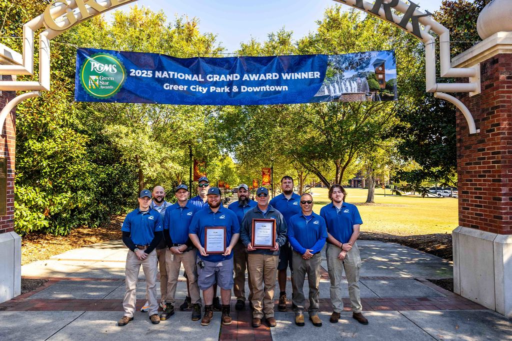 The City of Greer Urban Parks team pose for a photo under the Greer City Park entrance archway and award banner from PGMS