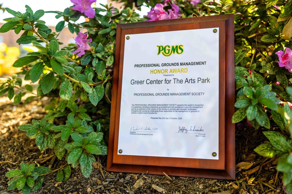 PGMS Honor Award for the Greer Center for the Arts Park propped up against a bush in Greer City Park