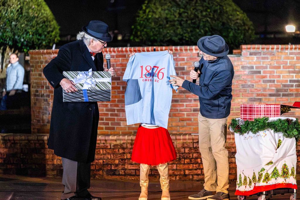 Greer150 Reveal at the Greer Christmas Tree Lighting - Mayor Danner, Museum Director David Lovegrove and the Mayor's Daughter hold up an 1876 Greer T-Shirt