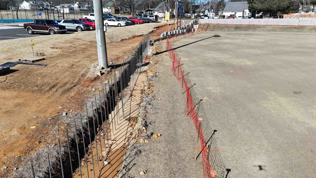 Drone shot showing rebar sticking out of the ground and a construction fence to the right of it