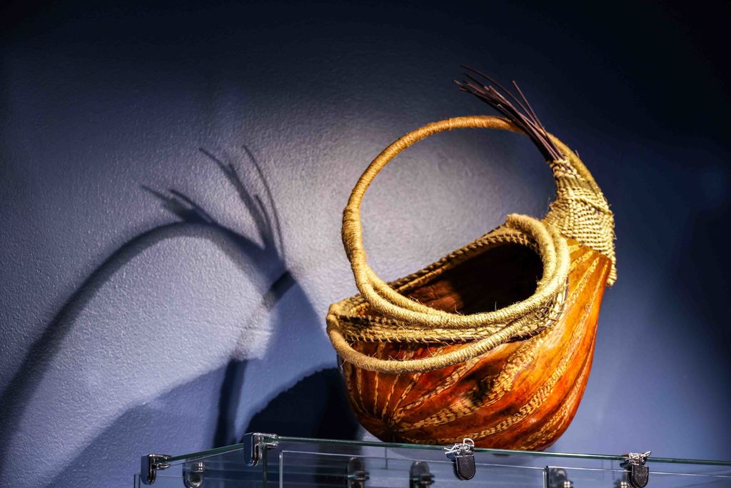 Close up shot of an artistic woven basket on top of a glass case with a blue wall backdrop