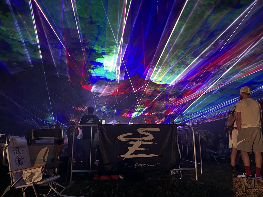 Multiple colorful laser lights radiate out from a stage with onlookers in the crowd