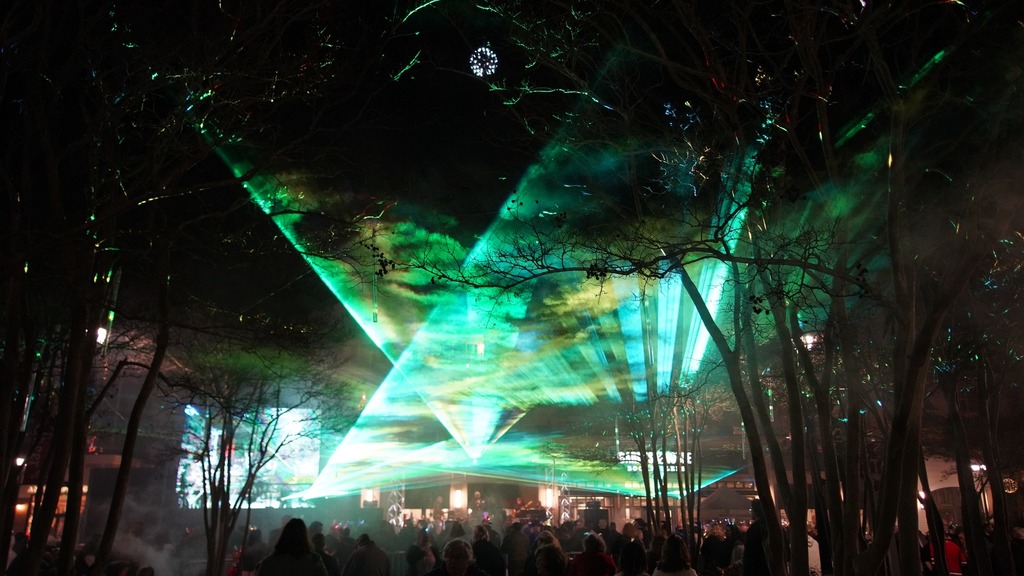 Multiple green laser lights radiate out from a stage with onlookers in the crowd