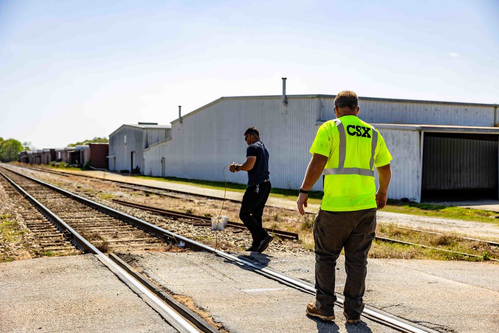 Two railroad workers stand over railroad tracks making measurements