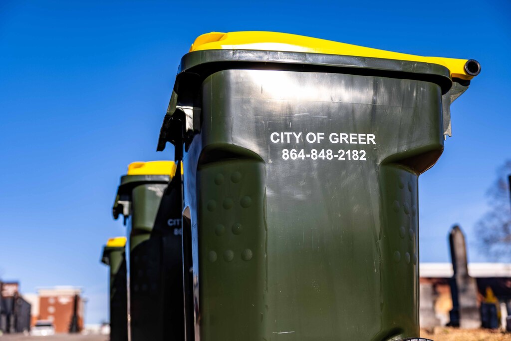 picture shows a row of green City of Greer trash cans