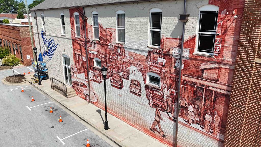 Artist paints Greer150 logo on wall while standing on lift