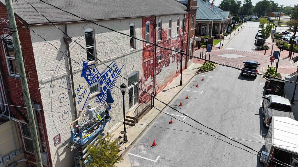 Artist paints Greer150 logo on wall while standing on lift