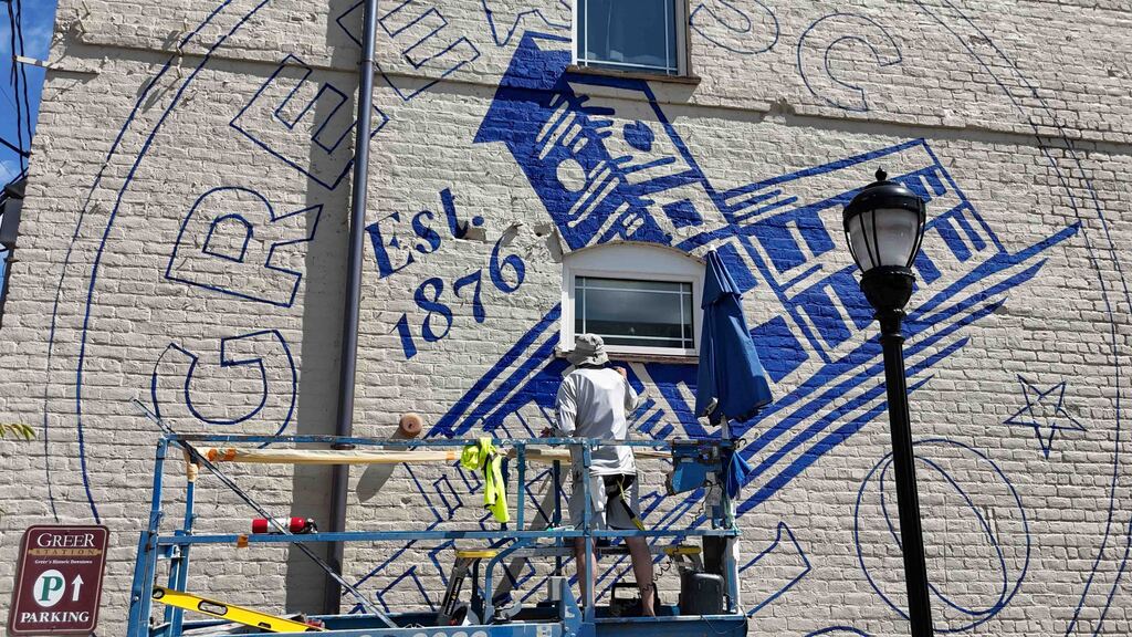 Artist paints Greer150 logo on wall while standing on lift